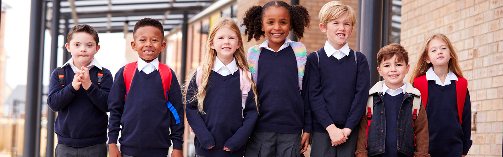 Primary school kids standing in a row on a walkway outside their school, smiling to camera, low angle